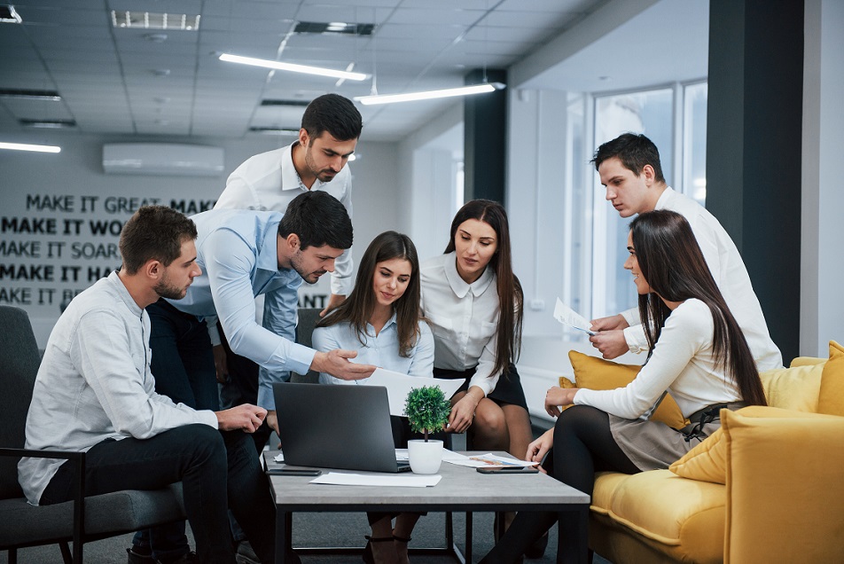 Guy shows document to a girl. Group of young freelancers in the office have conversation and working consulants informatique esn